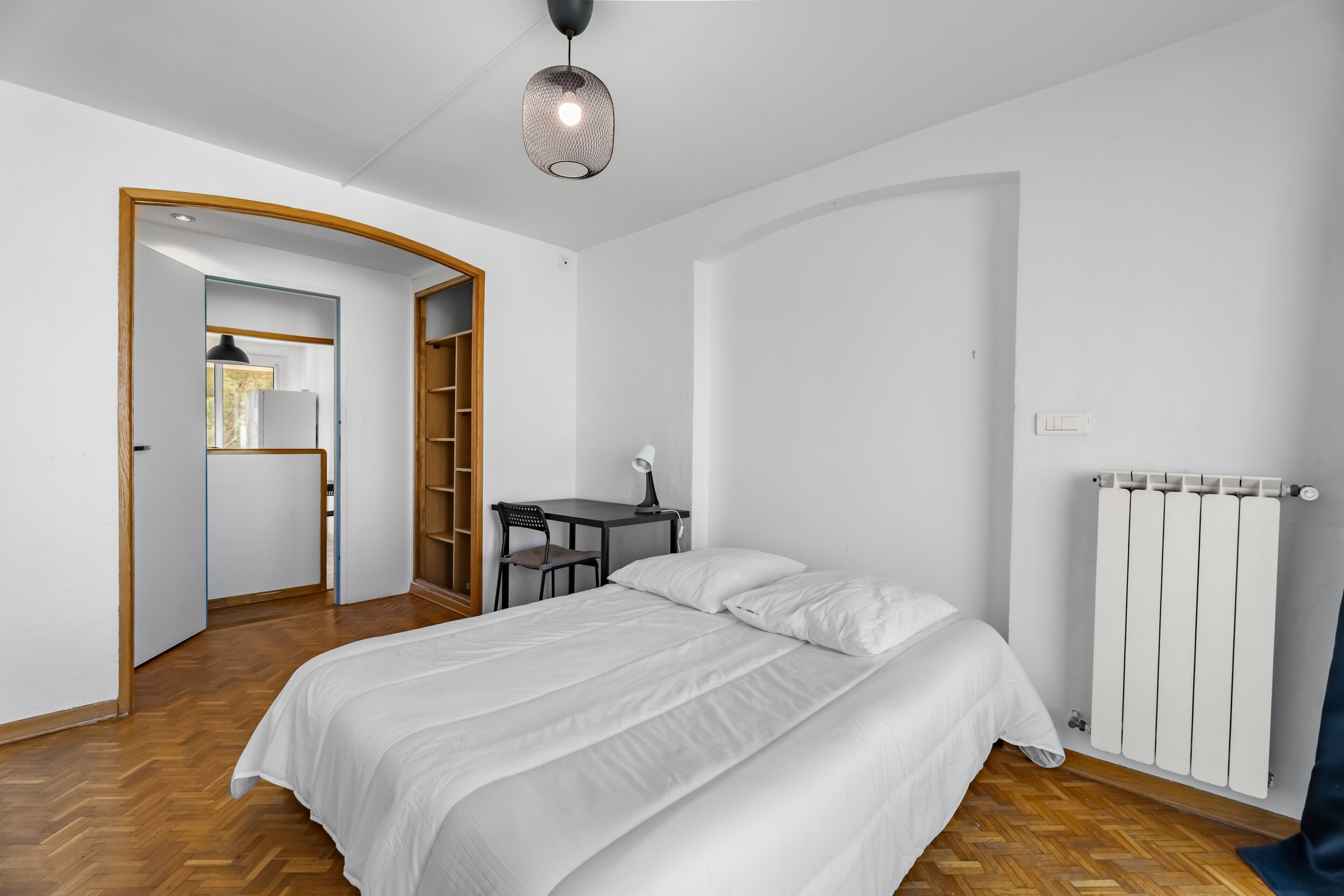 Een slaapkamer met een bed, een bureau, een stoel, een radiator en een kledingkast.