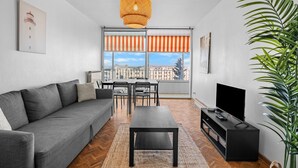 A modern living room with a sofa, dining table, chairs, a TV, and a large window with striped curtains. - Superb Apartment with Panoramic View – Sleeps 8 – Marseille 9th District (Marseille)