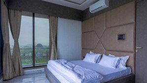 A bedroom with a large bed, a view through a window, and an air conditioning unit.