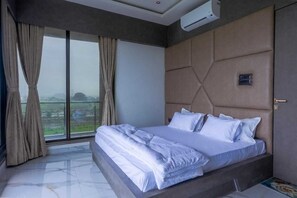 A bedroom with a large bed, a view through a window, and an air conditioning unit. - Pearl Drops Villa – Luxury Poolside Retreat Perfect for Parties & Getaways (Igatpuri)