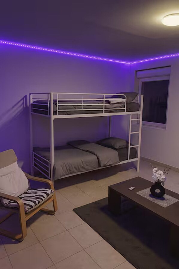 Un lit superposé avec un bureau et une chaise, une fenêtre et un éclairage à DEL de couleur violette.
