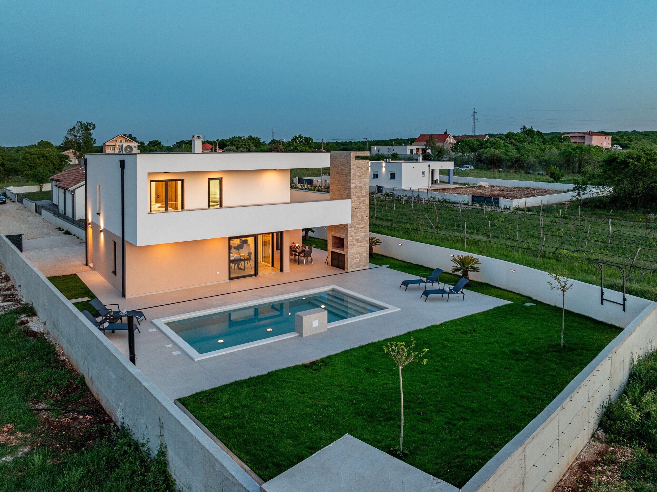 Ein modernes, zweistöckiges Haus mit Schwimmbad, Sitzgelegenheit im Freien und einem gepflegten Rasen.