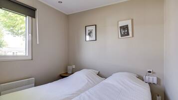 A bedroom with two beds, a window with a blind, a radiator, and two framed pictures on the wall.