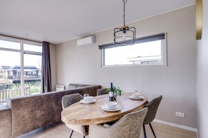 A dining area with a wooden table set for two, a bench, and a view of the outdoors. - Cube XL 72 | 4 persoons chalet in Zennewijnen (Zennewijnen)