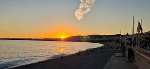 Sonnenuntergang an der Küste mit einer Promenade, Gebäuden und wolkenlosem Himmel.