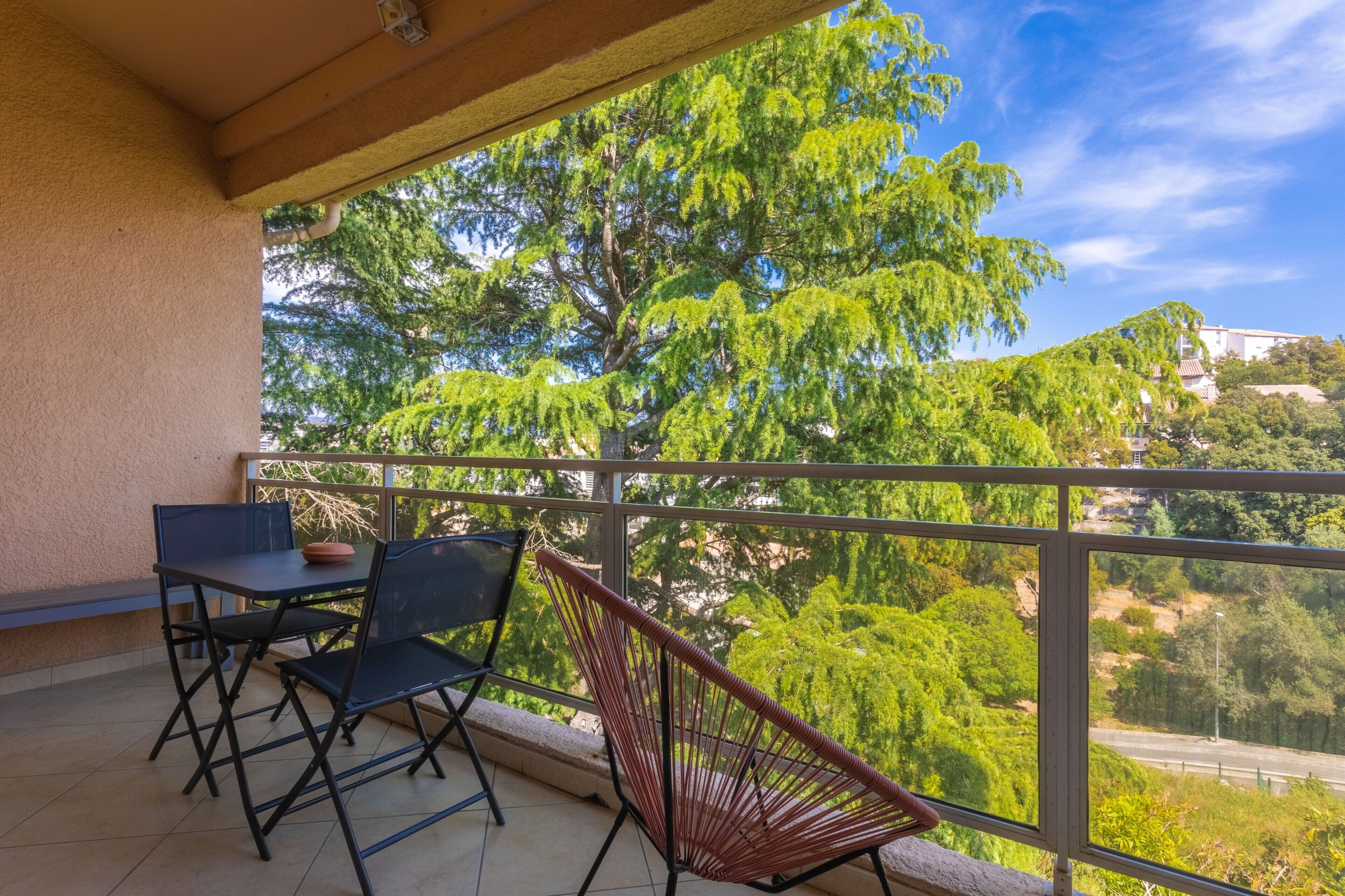 A balcony with a table and chairs, a hanging chair, and a view of trees and buildings.