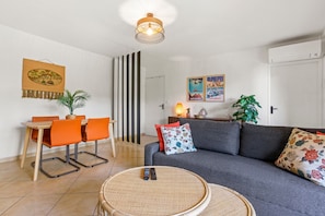 A living room with a sofa, chairs, a dining table, and a TV. - Apartment “Oasis Des Archers” with Shared Pool, Wi-Fi, and Air Conditioning (Saint-Raphaël)
