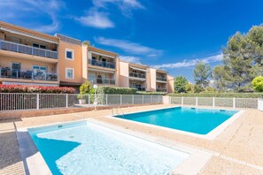A swimming pool with a white deck, surrounded by a white fence, and adjacent to a multi-story building with balconies. - Apartment “Oasis Des Archers” with Shared Pool, Wi-Fi, and Air Conditioning (Saint-Raphaël)