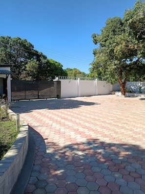 A paved walkway with hexagonal tiles, a metal fence, and a tree. - Tiptree Lodge (Livingstone)