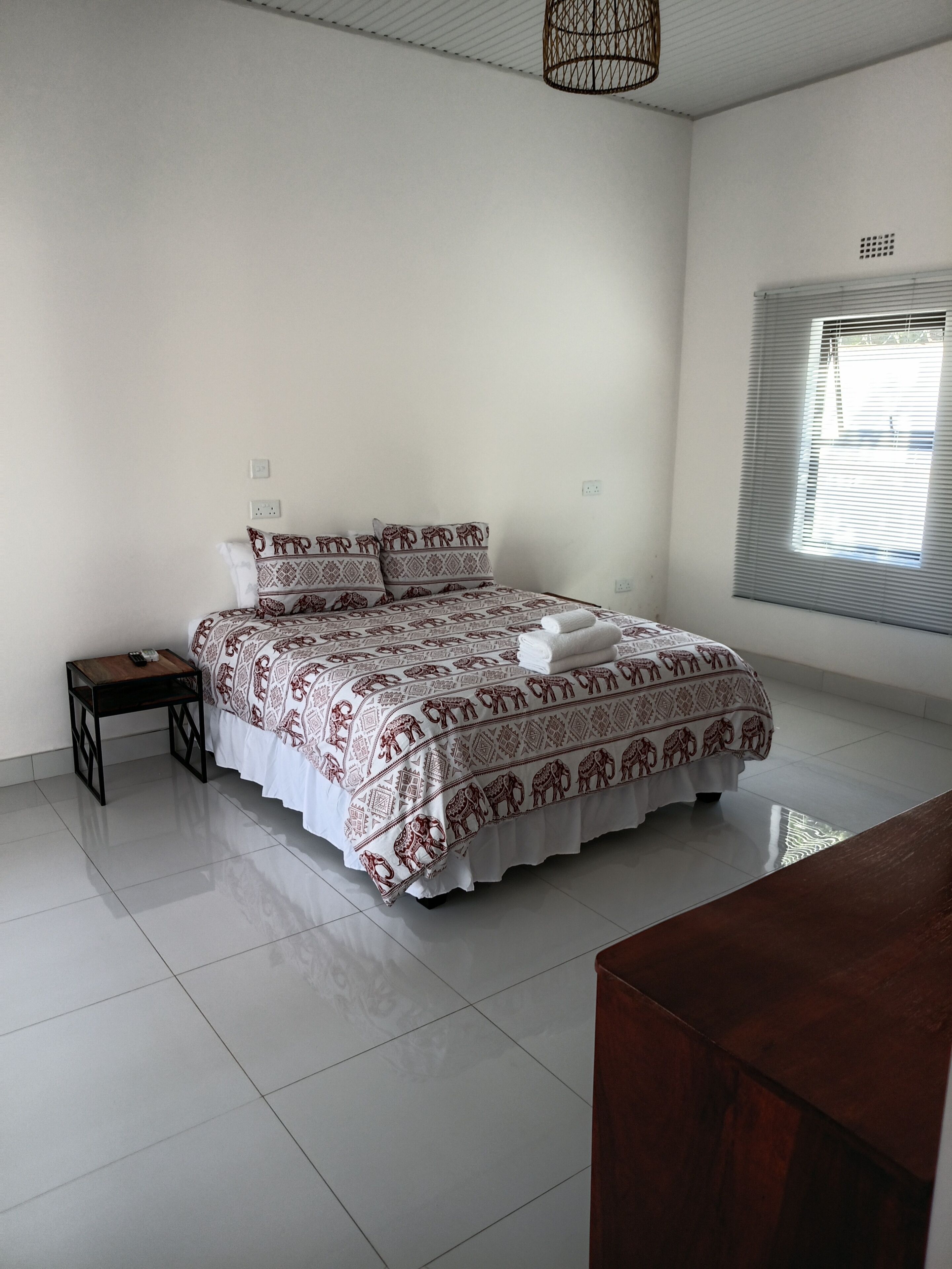A bedroom with a bed, bedside table, and a window with blinds.