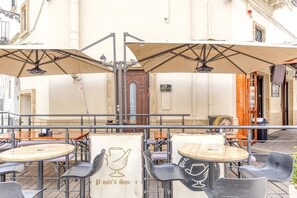 Un caffè all'aperto con tavoli, sedie, ombrelloni e una porta in legno sullo sfondo.