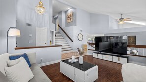 A modern living room with a sofa, coffee table, TV, and staircase. - 20% OFF Monthly  Mountain View & Huge Backyard & Hot Tub - 3 King Bed (Pomona)