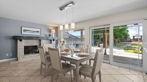 A dining area with a fireplace, a table set for four, and a view of the backyard. - 20% OFF Monthly  Mountain View & Huge Backyard & Hot Tub - 3 King Bed (Pomona)