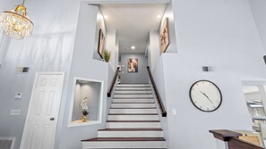 A staircase with a clock, a door, and a chandelier. - 20% OFF Monthly  Mountain View & Huge Backyard & Hot Tub - 3 King Bed (Pomona)