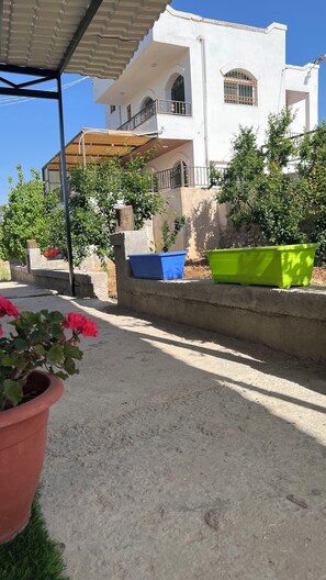 A white building with balconies, a concrete pathway, and potted plants.