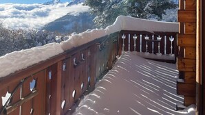 A wooden balcony with snow-covered railings and a clear view of snow-capped mountains.