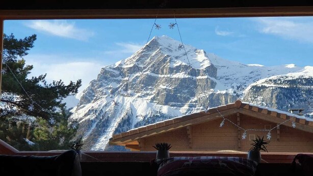 A mountain view from a wooden cabin with a clear sky.