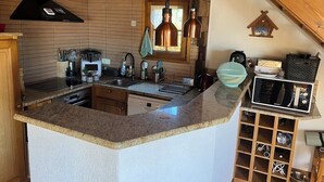 A kitchen with a granite countertop, stainless steel appliances, wooden cabinets, and a hanging light fixture.