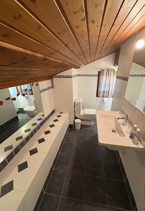 Une salle de bain avec un plafond en bois, une baignoire, des toilettes et un lavabo.