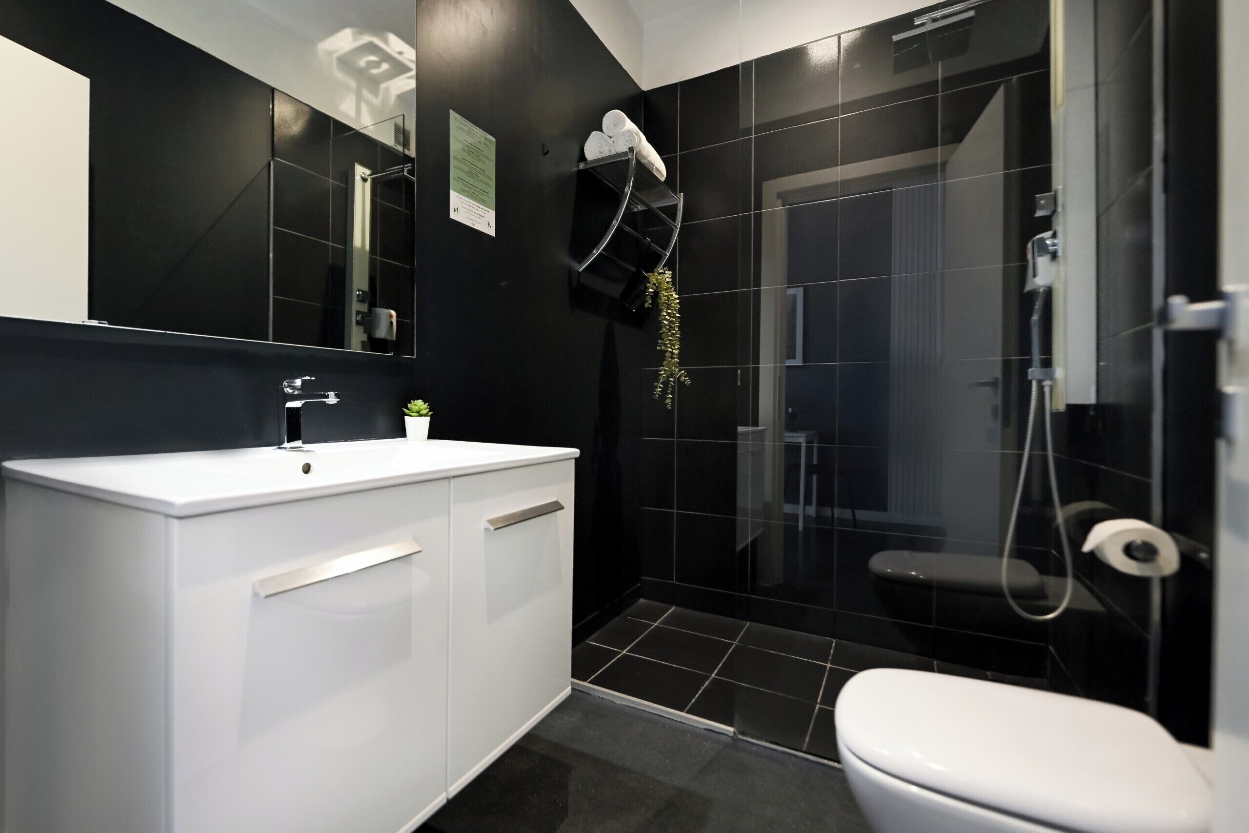 Un baño moderno con tocador blanco, cabina de ducha de vidrio y pared revestida de baldosas negras.