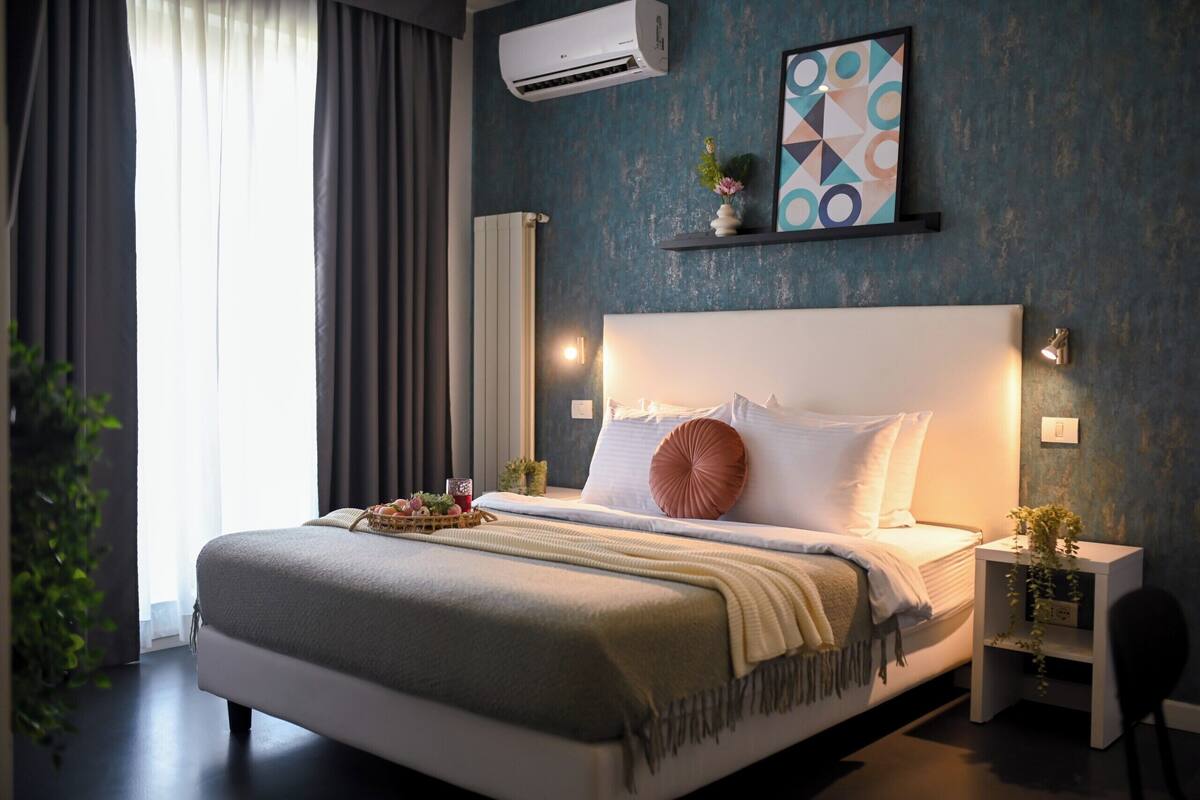 Un dormitorio moderno con una cama grande, mesitas de noche, aire acondicionado de pared y una obra de arte geométrica en la pared.