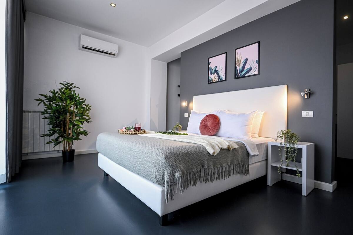 Un dormitorio moderno con una cama grande, mesitas de noche, una planta en maceta y obras de arte en la pared.