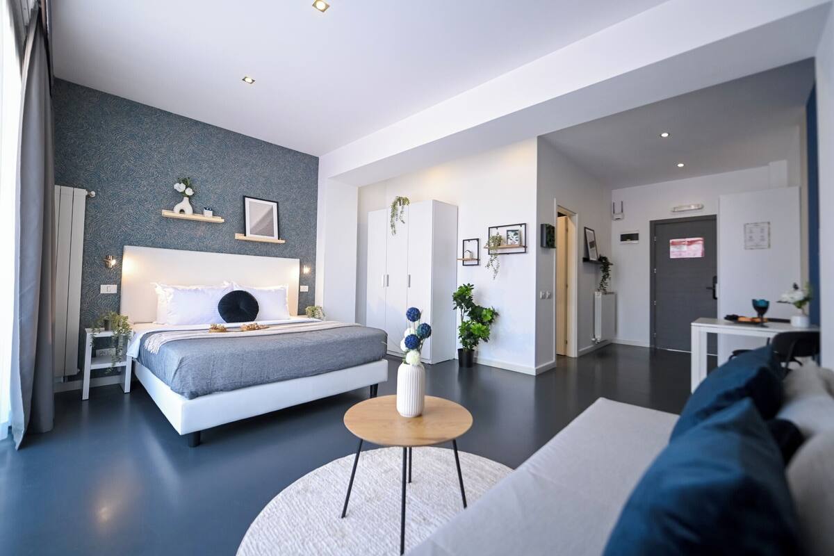 Un dormitorio moderno con cama, mesitas de noche, una mesa de centro redonda y una zona de estar con sofá.