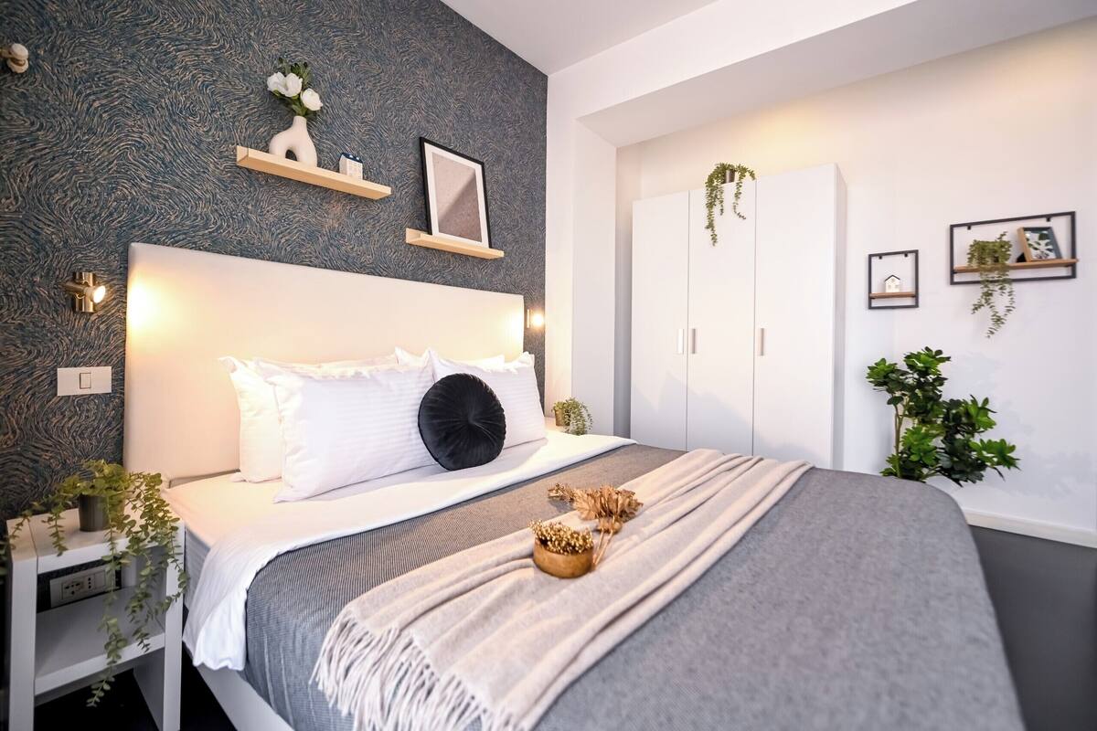 Un dormitorio moderno con cama, mesitas de noche, un armario y detalles decorativos en la pared.