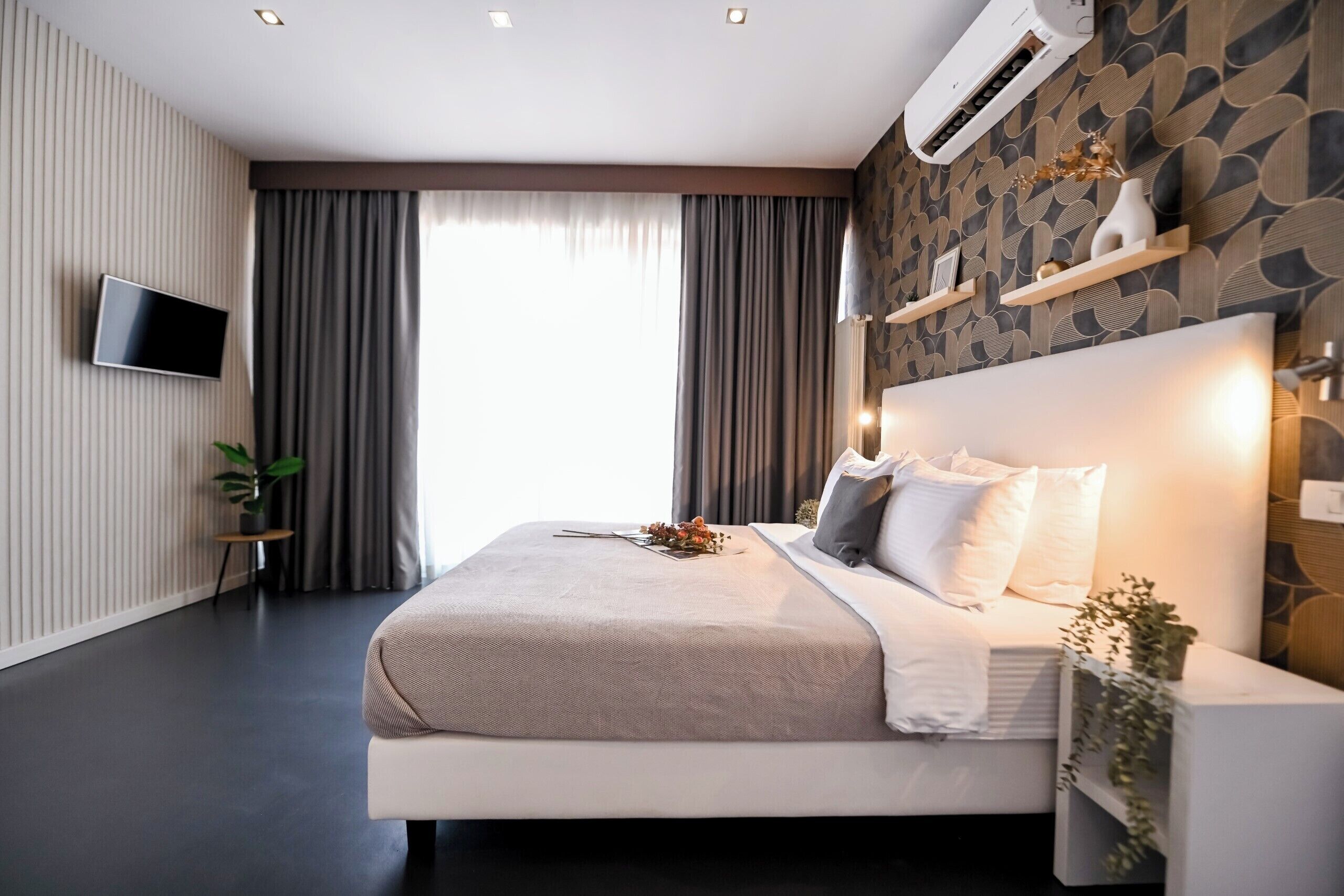 Une chambre moderne avec un grand lit, un téléviseur à écran plat, un climatiseur fixé au mur et une fenêtre avec des rideaux.
