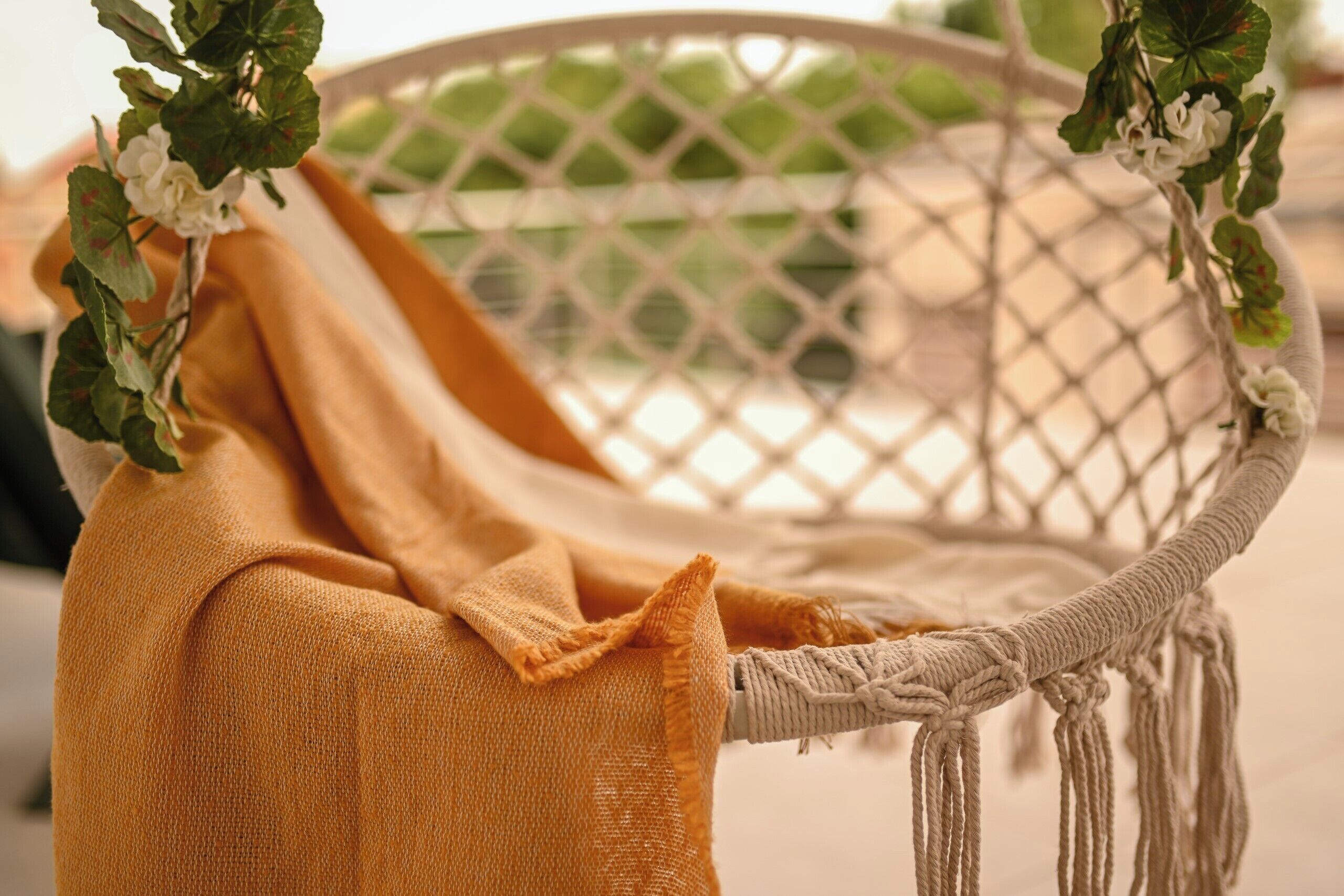 Une chaise en osier agrémentée de détails en macramé et recouverte d’un tissu jaune.