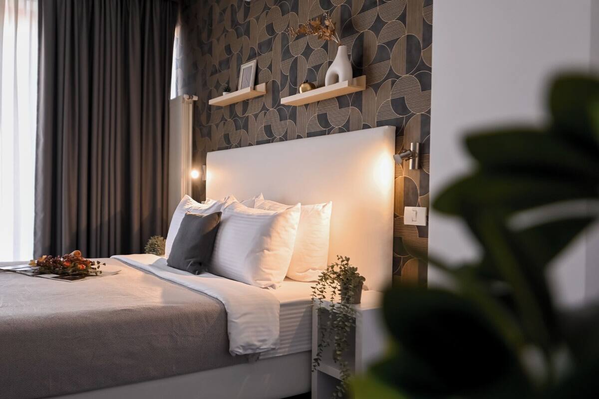 Una cama bien tendida con almohadas, una planta en la mesita de noche y una pared con estampado geométrico.