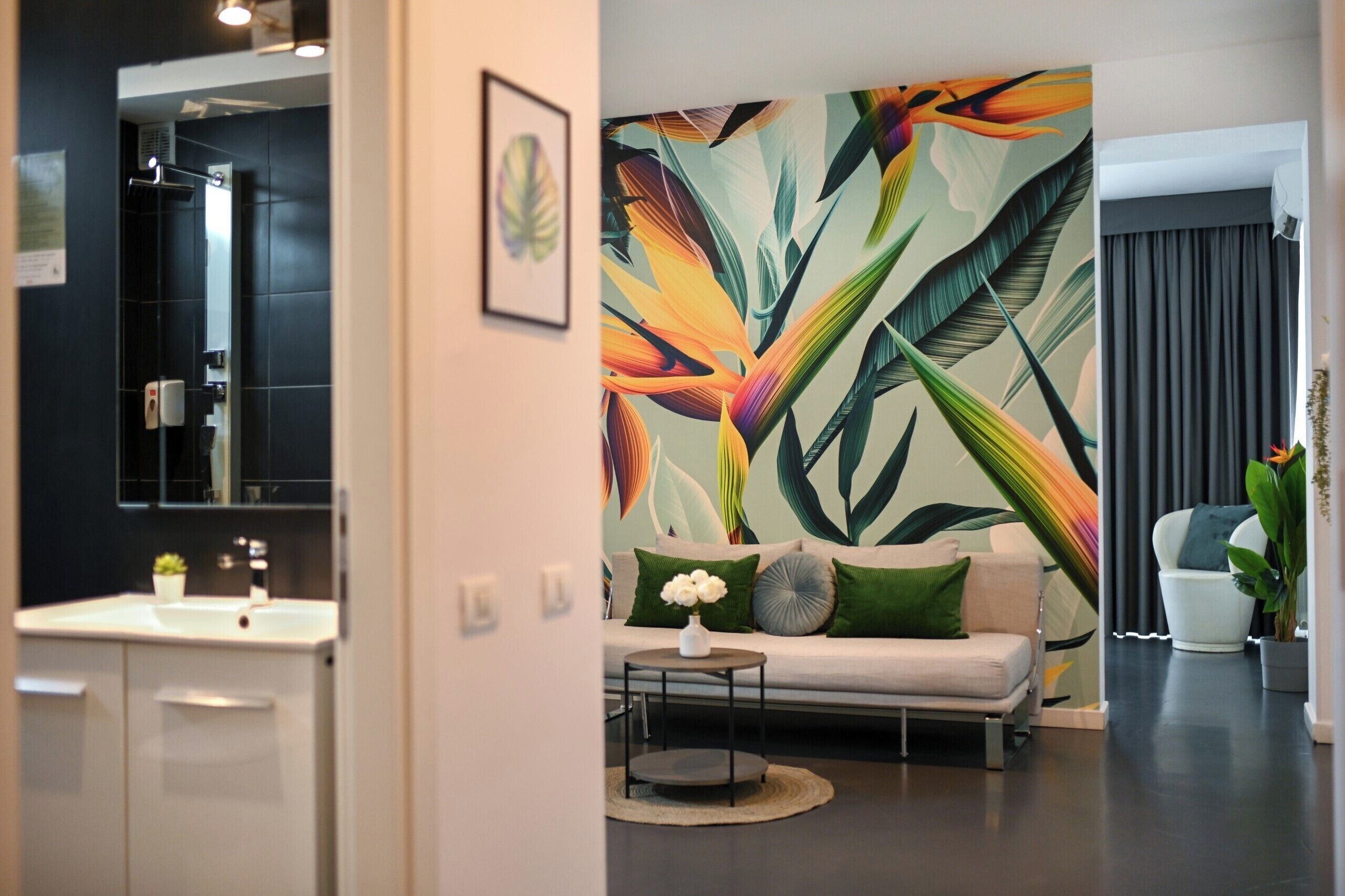 Un salon moderne agrémenté d’une grande fresque murale représentant des feuilles tropicales, d’un canapé blanc, d’une table basse ronde et d’une plante en pot.