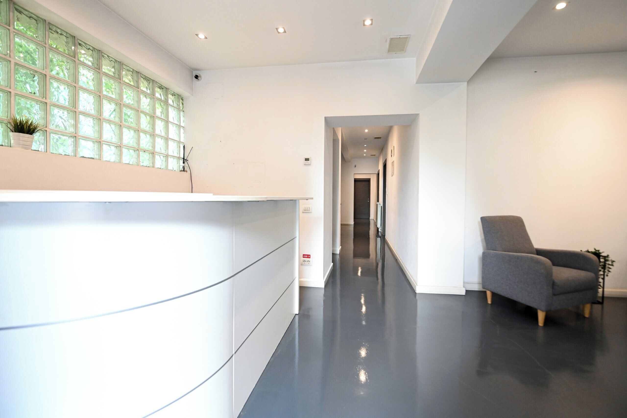 Eine moderne Hotelhalle mit einer Rezeption, einem grauen Sessel und einem Flur zu weiteren Zimmern.