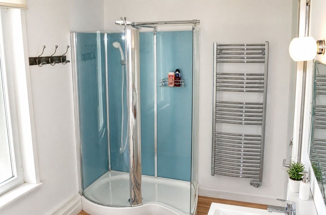 A shower with a glass enclosure, a towel rack, and a small shelf with toiletries.