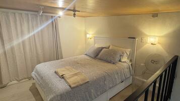 Un dormitorio con una cama, dos luces fijadas a la pared, un ventilador de techo y suelo de madera.