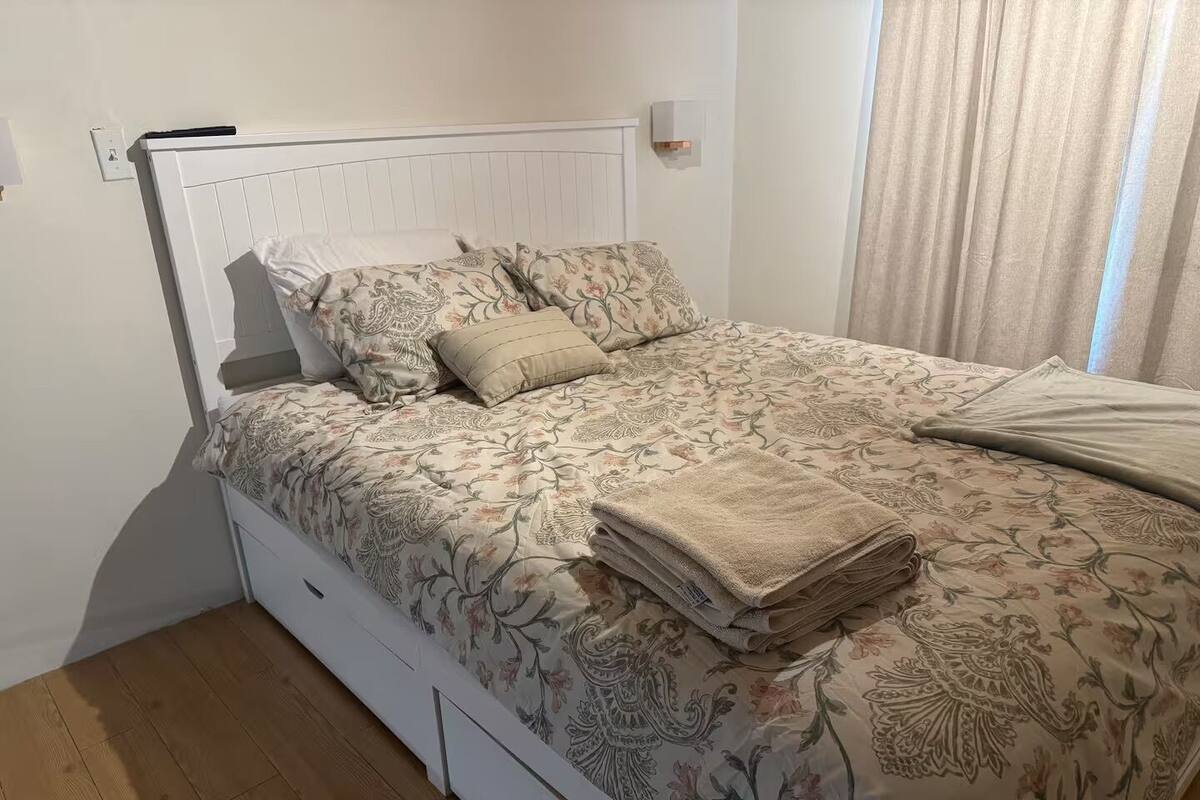 A bed with a floral bedspread, a beige pillow, and a folded blanket on a white headboard.
