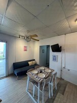 Un comedor con una mesa dispuesta para cuatro, un sofá, un ventilador de techo y un televisor montado en la pared.