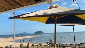 Escena de playa con una estructura de madera, una sombrilla y vista al mar y una isla distante.