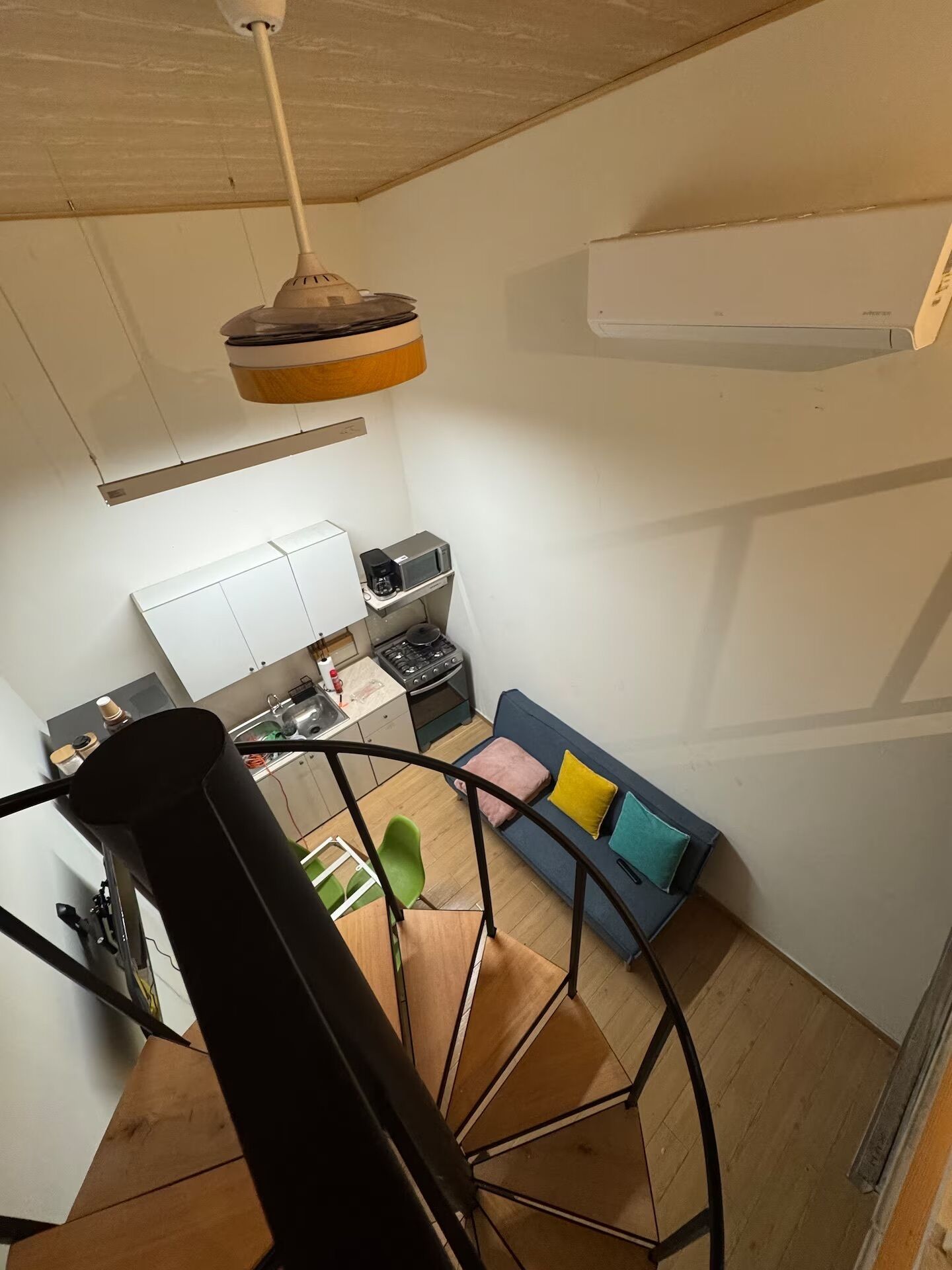 A modern kitchen with a built-in stove, a dining area with a blue sofa and colorful cushions, and a staircase leading to another level.