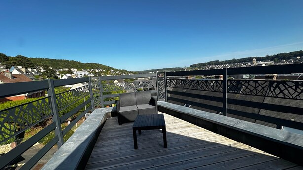 A wooden deck with a bench and a table, overlooking a residential area with houses and a hill in the distance. - Captain YOO - A Stopover in Fécamp: Terrace with Ocean View (Fécamp)