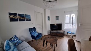 A living room with a sofa, armchair, TV, and artwork on the wall. - Captain YOO - A Stopover in Fécamp: Terrace with Ocean View (Fécamp)