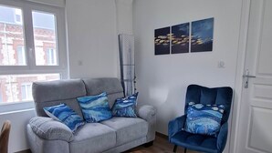 A living room with a grey sofa, a blue armchair, a wooden coffee table, and a modern pendant light. - Captain YOO - A Stopover in Fécamp: Terrace with Ocean View (Fécamp)