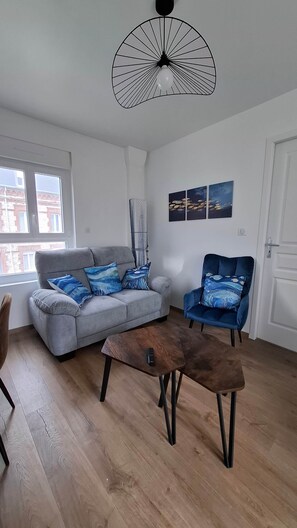 Ein Wohnzimmer mit grauem Sofa, blauem Sessel, Couchtisch aus Holz und einer modernen Pendelleuchte.