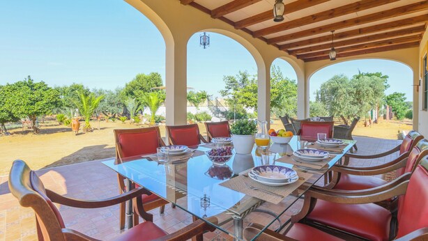 A covered outdoor dining area with a table set for six, surrounded by red chairs, and a view of the vineyard in the background. - Holiday Home Los Miradores, Marchena, Seville (Marchena)