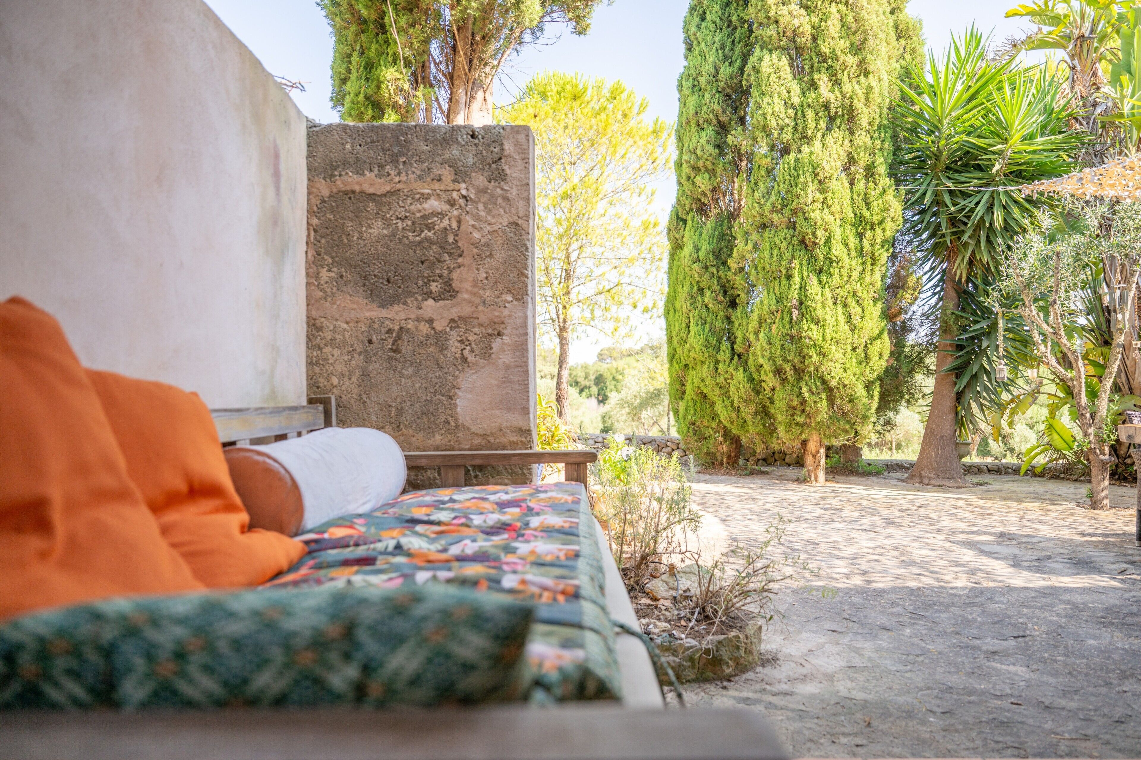 A bed with an orange blanket, a stone wall, and a garden with trees and plants.