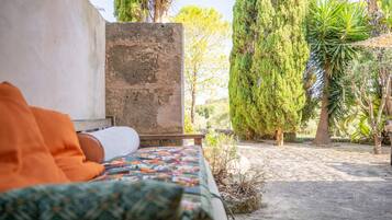 A bed with an orange blanket, a stone wall, and a garden with trees and plants.