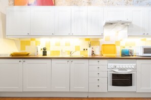 Una cocina con armarios blancos, microondas, horno y salpicadero con azulejos amarillos.