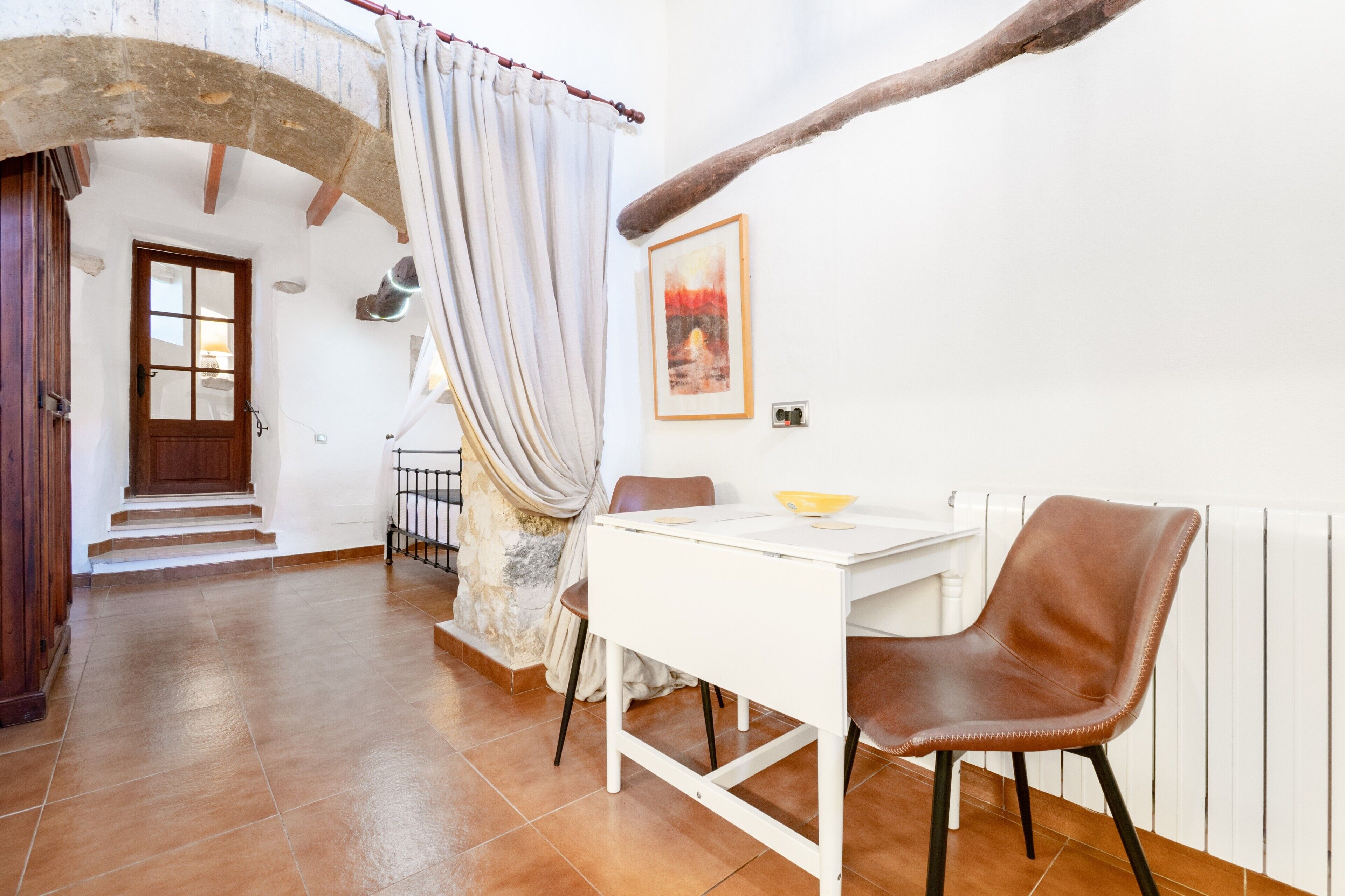 Un comedor con una mesa blanca y sillas marrones, un arco de piedra y un cuadro en la pared.