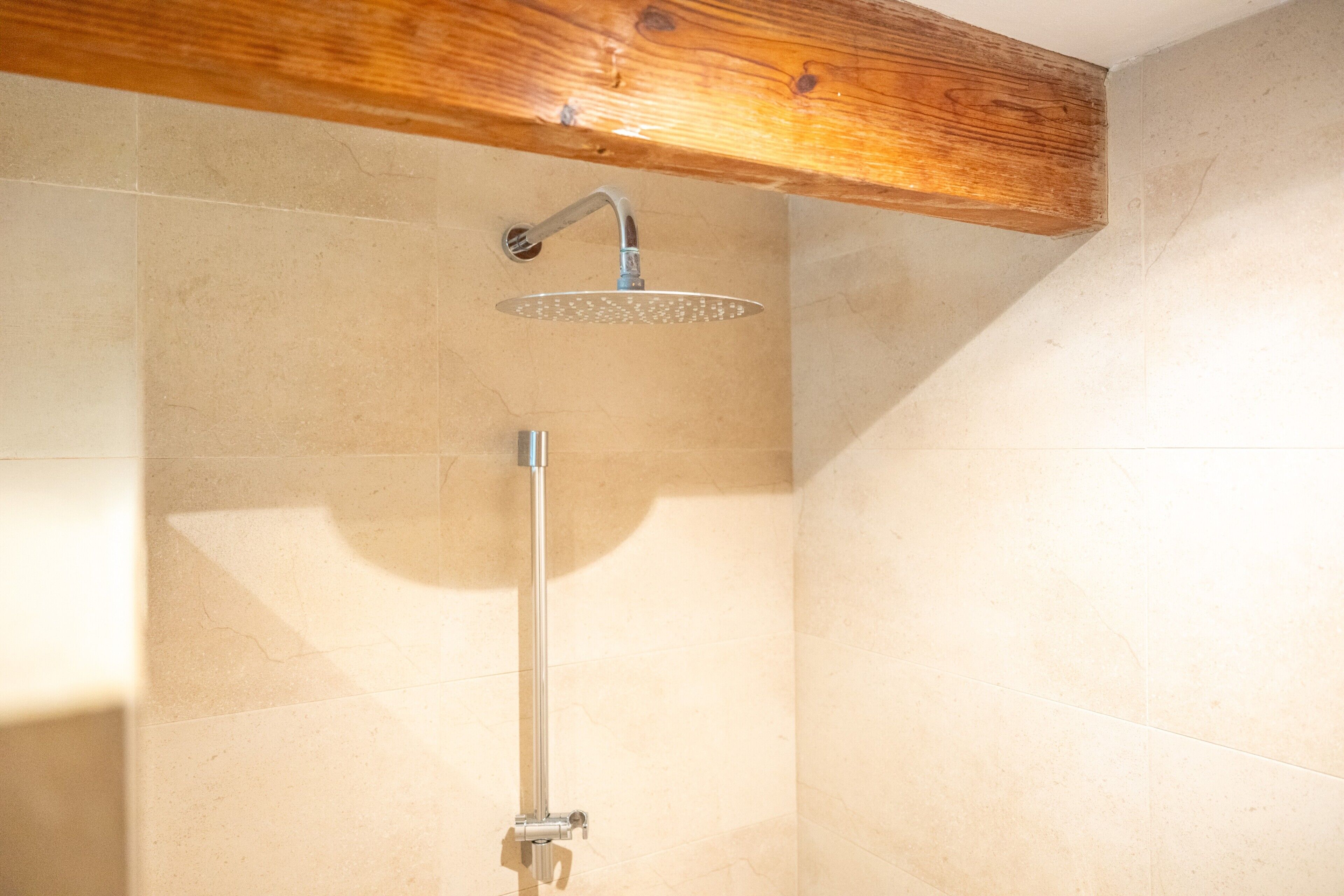 Ducha con viga de madera en el techo, un cabezal de ducha y un rociador de mano.