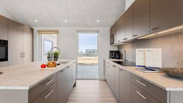 Une cuisine moderne dotée d’un grand îlot central, d’un four encastré et offrant une vue par la fenêtre.
